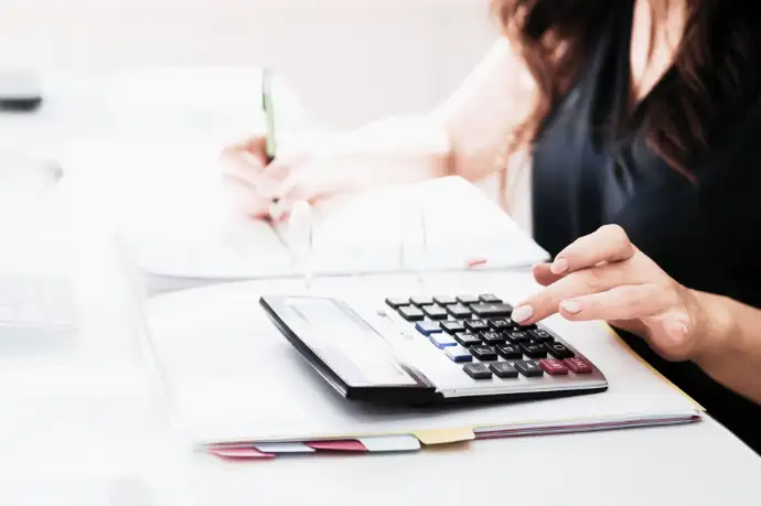Profesional de asesoría contable haciendo cálculos con calculadora y tomando notas en su escritorio