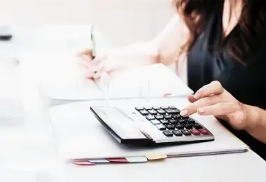 Profesional de asesoría contable haciendo cálculos con calculadora y tomando notas en su escritorio